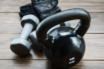 Fototapeta na wymiar Black kettlebell, grey dumbbells and workout gloves on dark floor. Weight lifting exercise concept. Gym and fitness background.