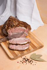 Sliced baked pork with herbs and spice on wooden board.