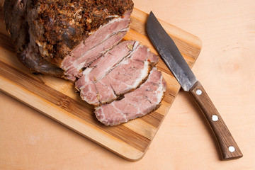 Sliced baked pork with herbs and spice on wooden board.