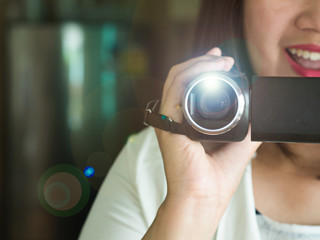 Happy smiling woman with hand holding video camera or camcorder recording some happy events coming in her life with beautiful lens flare
