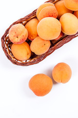 Several of harvested apricots in basket with whole and halved apricots on white background..