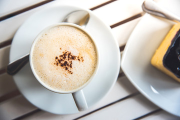 A cup of latte, cappuccino or espresso coffee on a white wood table and a Blueberry Cheesecake.