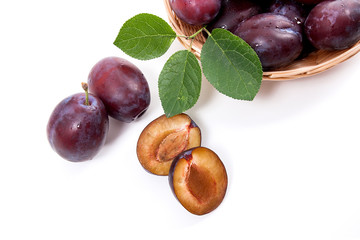 Yellow wooden basket with ripe plums, whole and half ripe plums isolated on a white background..