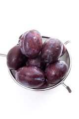 Steel colander with ripe plums isolated on a white background..