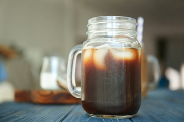 Mason jar with cold brew coffee and ice on wooden table