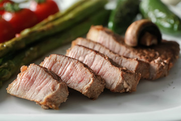 Sliced steak with vegetables on white plate, closeup