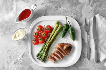 Sliced steak on white plate served with vegetables and sauces
