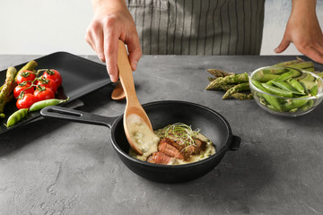 Man adding sauce to sliced steak on frying pan