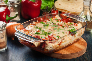 Traditional mexican enchiladas with chicken meat, spicy tomato sauce and cheese in heat resistant...