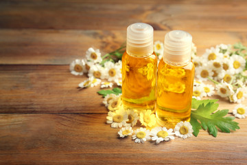 Bottles of chamomile oil with fresh flowers on wooden background