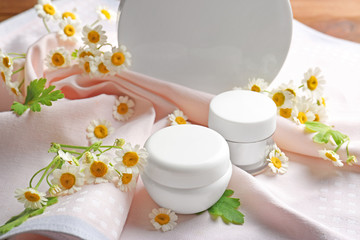 Chamomile cosmetic products with fresh flowers and fabric on table