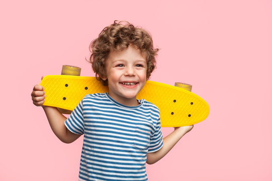 Cheerful boy with longboard on pink