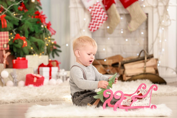 Cute little baby with toys in room decorated for Christmas