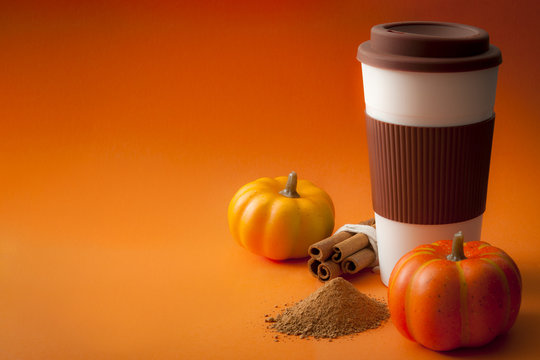 Fototapeta Seasonal coffee beverages and pumpkin spiced latte concept with a takeaway paper cup on orange background surrounded by cinnamon sticks and pumpkins with copy space for text