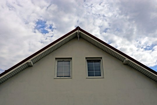фасад серого дома с маленькими окнами на фоне неба и облаков