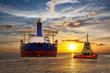 Tanker and tugboat on sea at sunset.