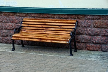 коричневая деревянная лавочка на тротуаре у каменной стены