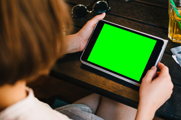 Crop shot of brunette sitting at table in cafe and holding tablet with green screen. 