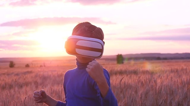 A boy stands in a wheat field at sunset in virtual glasses