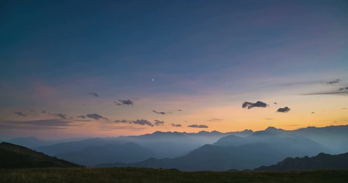 Day to night time lapse from high up on the Alps. Colorful sunset over mountain peaks and fog in the valleys below, moving clouds, setting moon and rotating stars.