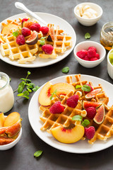 Homemade Belgian waffles with peach, raspberry, fig and honey on brown wooden background. Selective focus