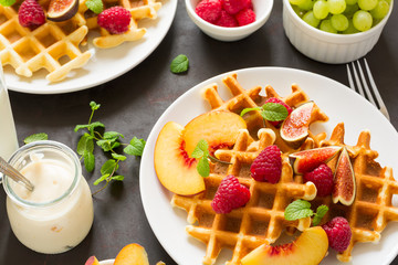 Homemade Belgian waffles with peach, raspberry, fig and honey on brown wooden background. Selective focus