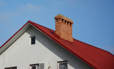 Close up on brick chimney with red metal tile roof. Roofing Construction.