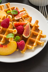Homemade Belgian waffles with peach, raspberry, fig and honey on brown wooden background. Selective focus