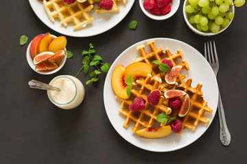 Homemade Belgian waffles with peach, raspberry, fig and honey on brown wooden background. Selective focus