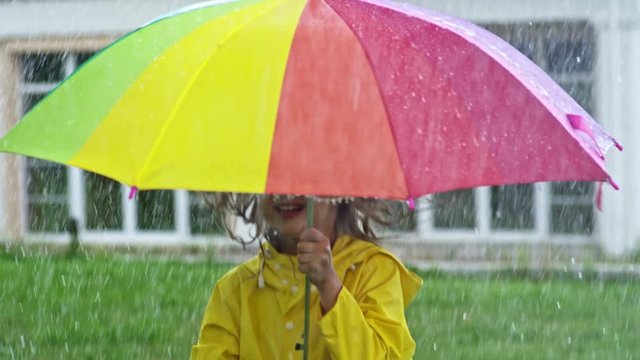 PAN of happy preschool little girls and boy holding colorful umbrellas and jumping on green grass during rain