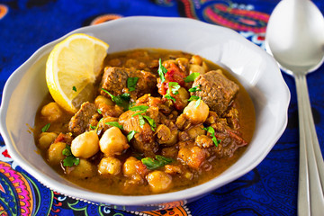 Moroccan soup harira with Meat Chickpeas Lentil Tomato Lemon and Spices in gray bowl. Arabic pattern background.