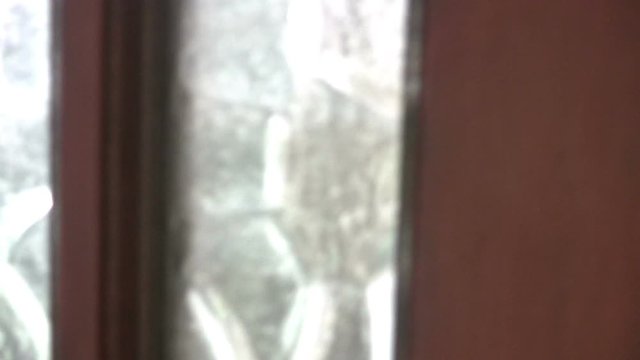 Close up interior shot of a man leaving a house by the  front door. The door has frosted glass panes and a Yale type lock.