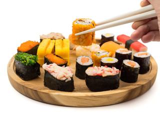 Hand holding sushi roll with chopsticks, Sushi set on wooden plate on white background, Japanese food.