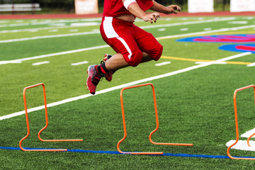 Football player jumping over orange hurdles,