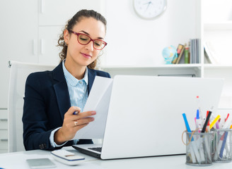 Young woman working with paperwork and laptop