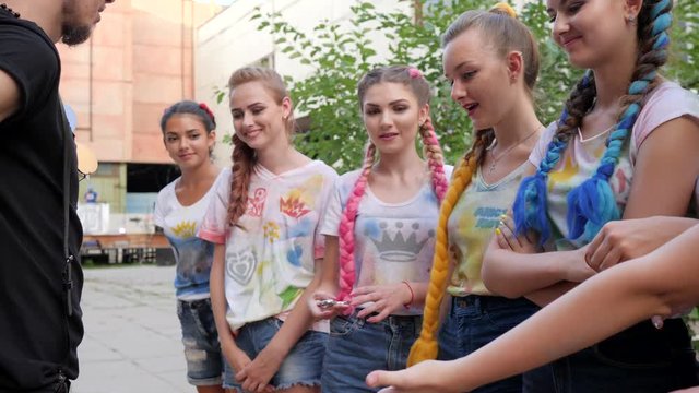 stylish girls standing on street with trendy braids with kanekalon, adolescents with bright hair at background of graffiti, girlfriends stand on open air take spinners into hands, fashionable toys