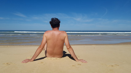 Naked man sit relaxing on sand at summer beach