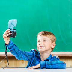 Young student in blue shirt make selfie at blackboard in school. Back to school concept background with copy space