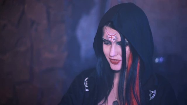 Portrait of woman with sly smile, dressed in fantasy overlord evil costume, wearing black cultist gown with ornament, yellow cats eye contact lenses. Shot with Sony a7s and Atomos Ninja Flame