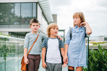 Obraz premium Group of 3 funny schoolkids posing outdoors, wearing backpacks. Back to school concept. Fashion for children