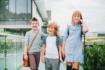 Group of 3 funny schoolkids posing outdoors, wearing backpacks. Back to school concept. Fashion for children