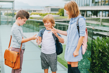 Group of 3 kids playing Rock, Paper, Scissors game on schoolyard. Back to school concept, fashion for children