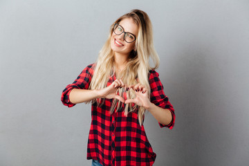 Cheerful young blonde woman showing heart gesture.