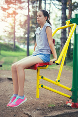 Fototapeta na wymiar Teenage girl doing exercises at simulator in park