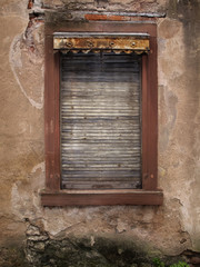 Altes Fenster in einer verwitterten Wand mit einem alten Holzrollladen.
