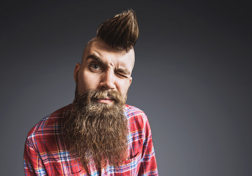 Excited trendy man portrait. Punk styled man with Mohawk hairstyle is smiling. Isolated on gray background