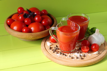 Fresh tomato juice in glass mugs. Mugs of tomato juice and fresh tomatoes on a green wooden background.