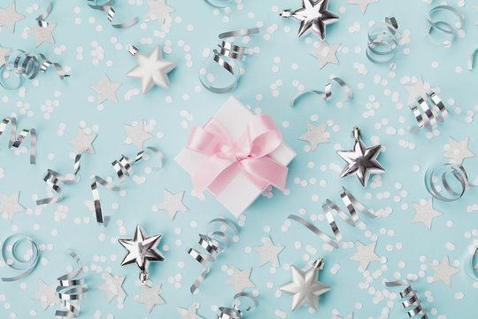 Gift Box On Blue Christmas Background Decorated Confetti And Silver Stars Top View. Flat Lay.