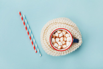 Cup of hot cocoa or chocolate wrapped in knitted scarf on blue table top view. Flat lay.