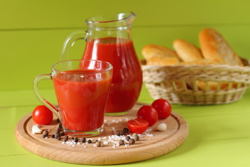 Fresh tomato juice in a glassware. A mug of tomato juice, fresh tomatoes and a baguette on a green...